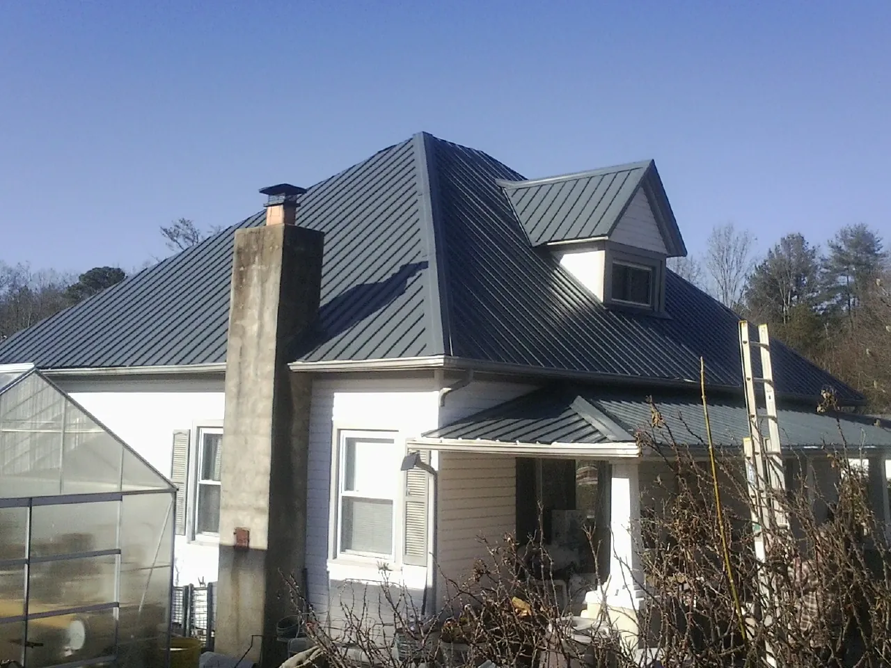 Dark blue standing seam metal roof on a white farmhouse with dormer — Slate & Tile Roof Repair by Roofing Brothers in Nuevo
