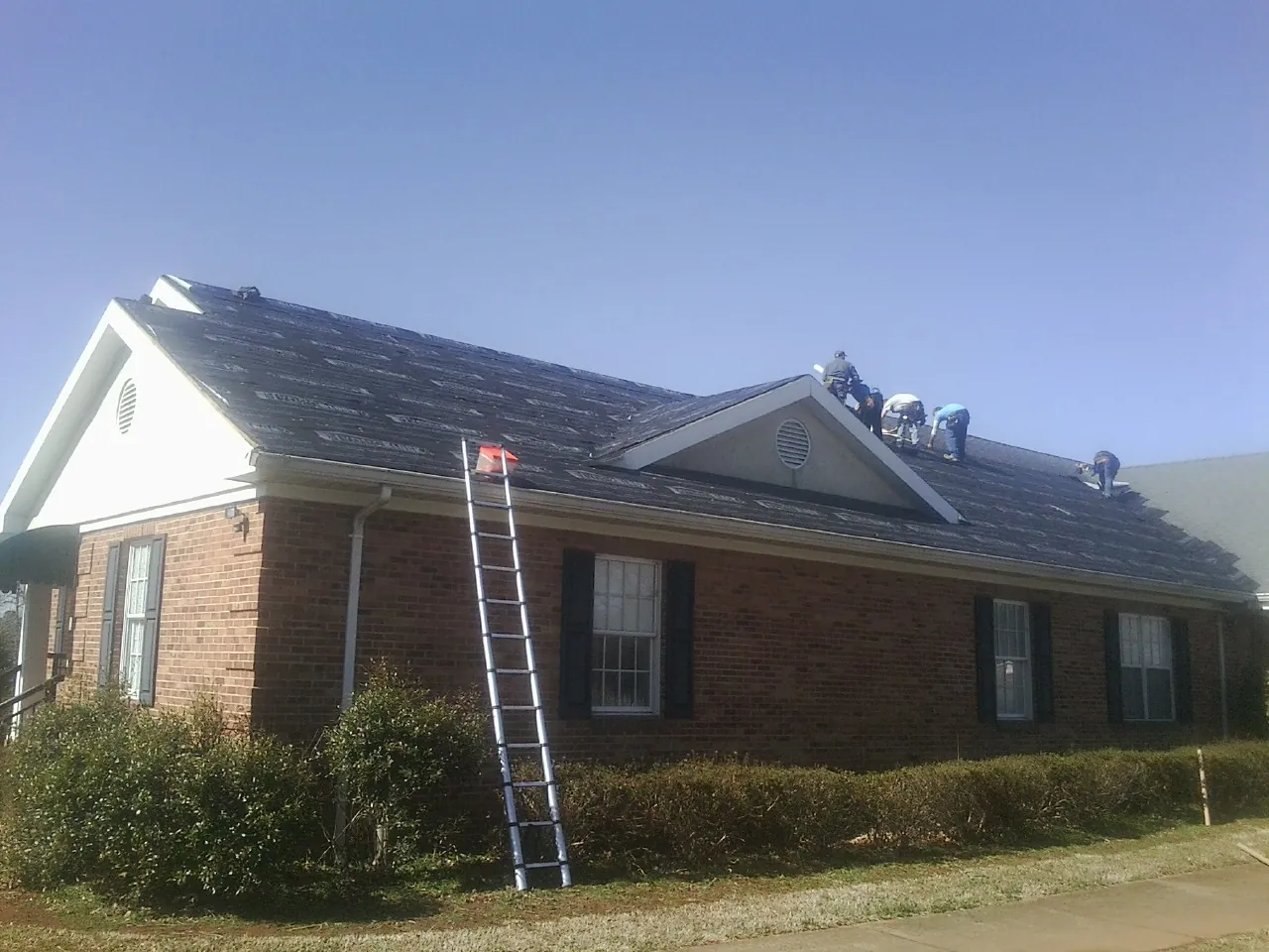 Crew tearing shingles off a brick ranch roof with a ladder set — Metal Roof Repair work by our crew in Nuevo
