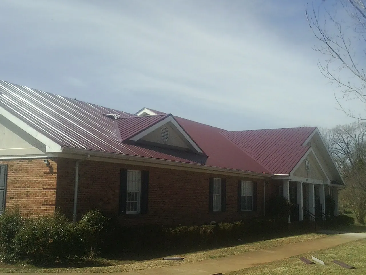 Red metal roof with gabled entries on a long brick building, from a Hail Damage Roof Repair job in Nuevo