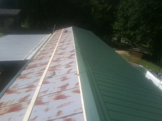 Old rusted panels beside newly installed green metal roofing — Wind Damage Roof Repair by Roofing Brothers in Nuevo