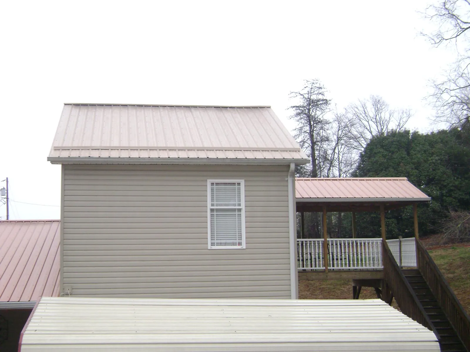 Tan metal roofs on a two story addition and attached porch, from a Roof Replacement job in Nuevo